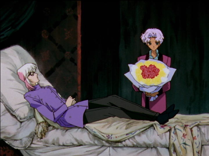 Mikage lying in a bed with large pillows and an old-fashioned look. Mamiya holds flowers.