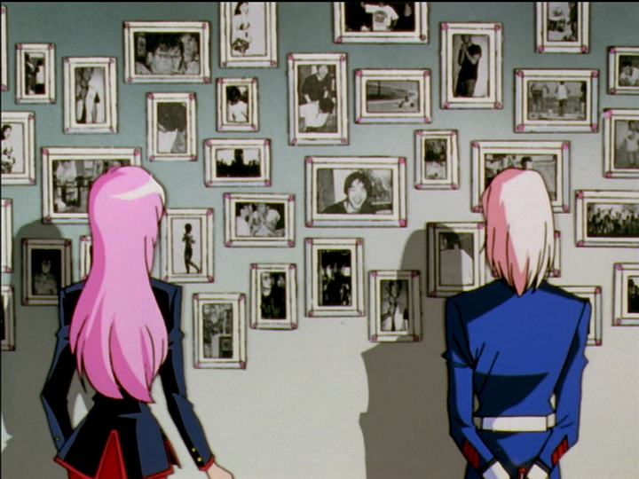 Utena and Mikage stand in front of Mikage’s photo wall.