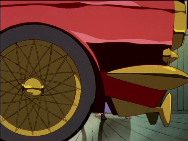 Akio’s car arrives. We see its front wheel and bumper.
