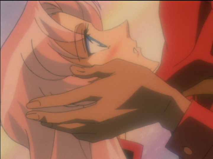 Akio’s hands are around Utena’s face and she is blushing as she looks up at him.