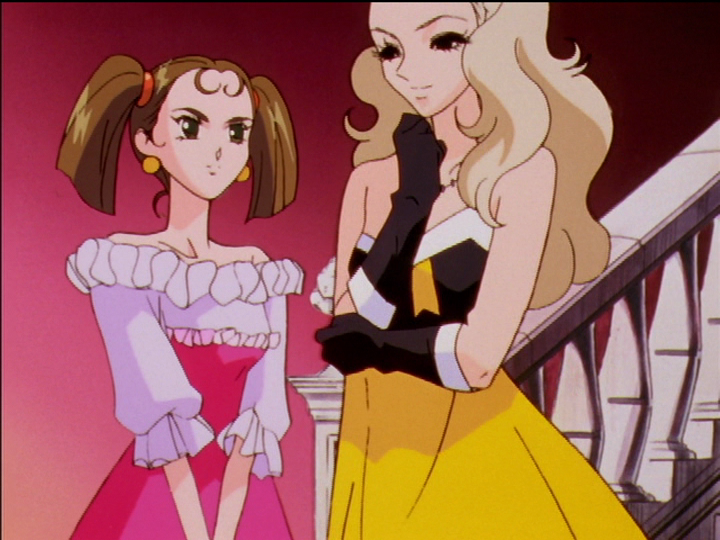 Nanami, wearing yellow with long black gloves, has descended the stairs and speaks to Keiko at the bottom.