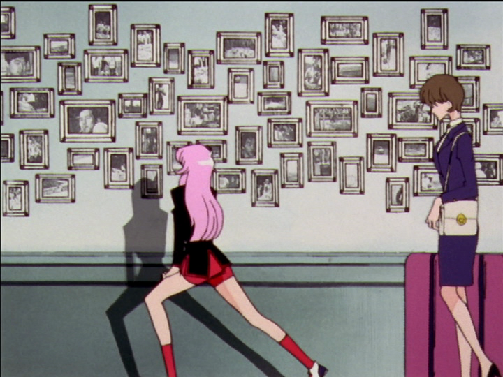 Utena stretches and Tokiko walks by Mikage’s photo wall.